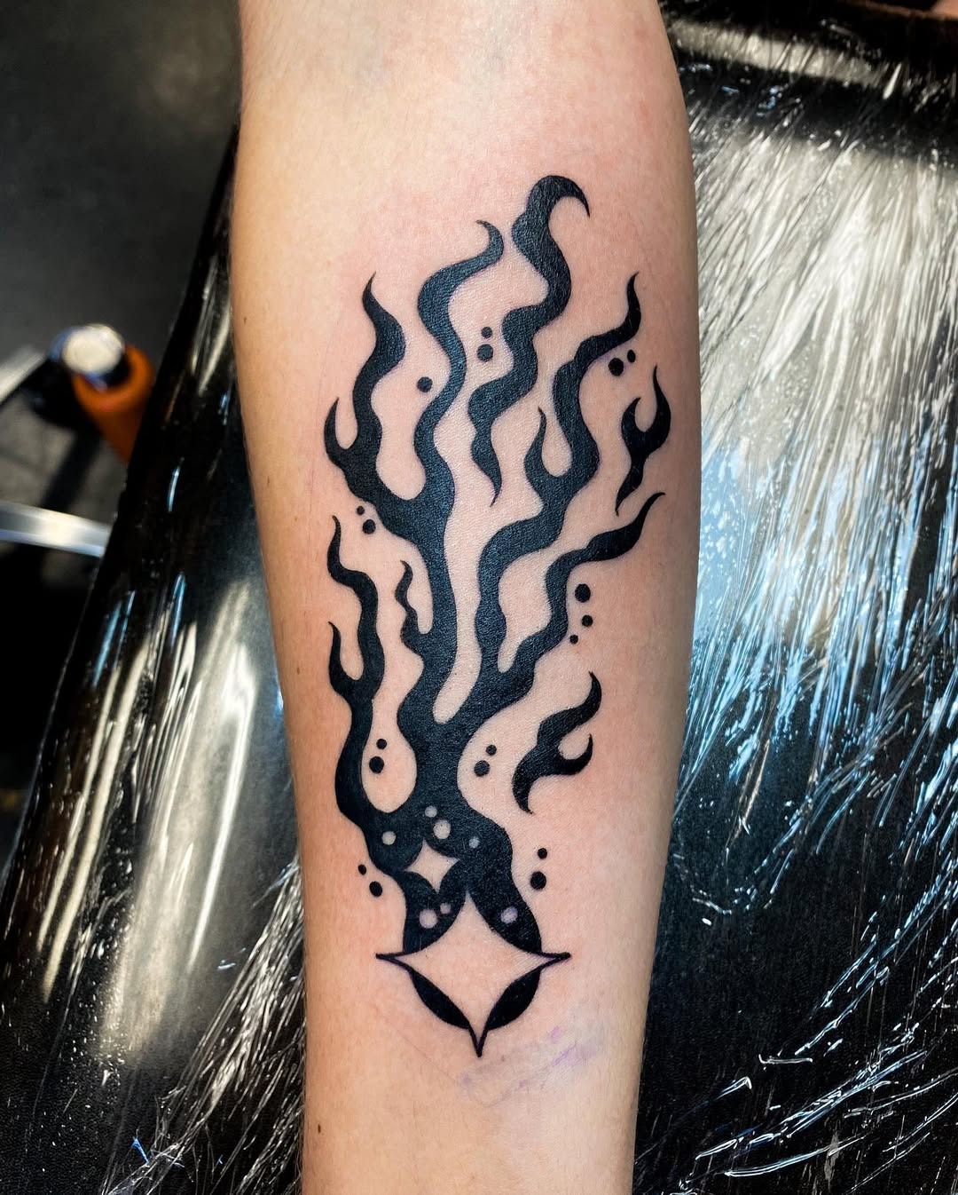 This tattoo features bold black ink swirling in an abstract flame design, evoking a sense of movement and energy.