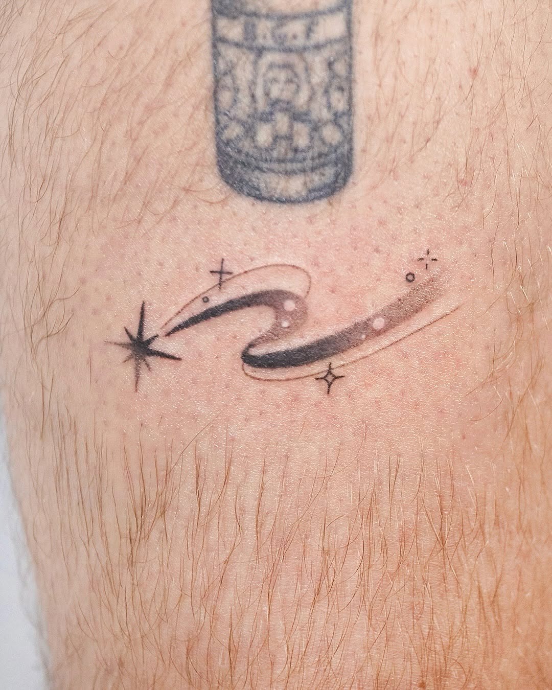 This tattoo showcases a sleek, minimalist meteor design with a shimmering starburst effect.