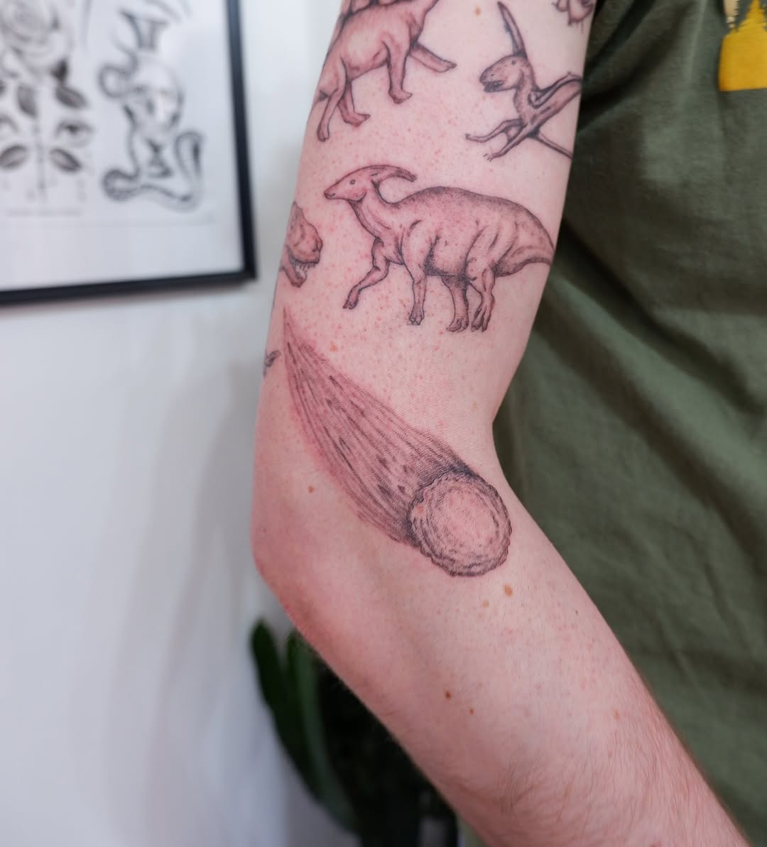 This tattoo features a captivating meteor design alongside playful illustrations of dinosaurs.