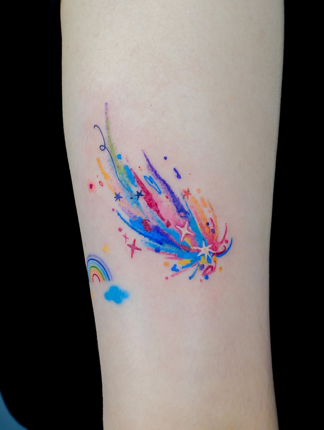 This tattoo features a stunning watercolor meteor bursting with colors and dynamic movement.
