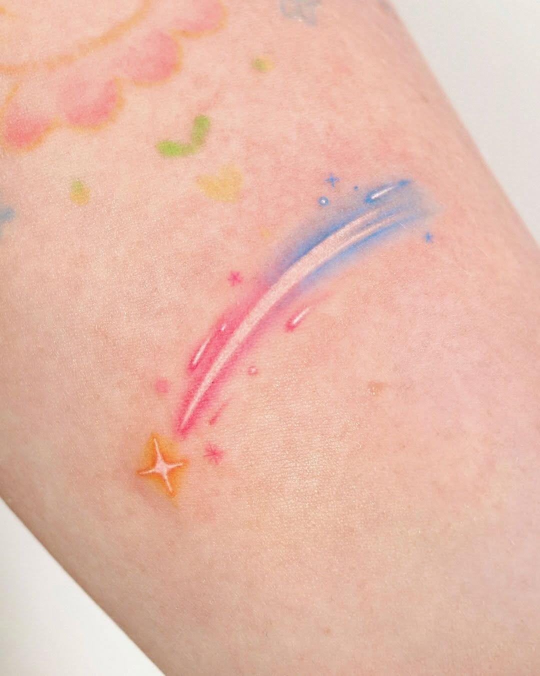 This tattoo features a colorful meteor streak with soft pastel hues.