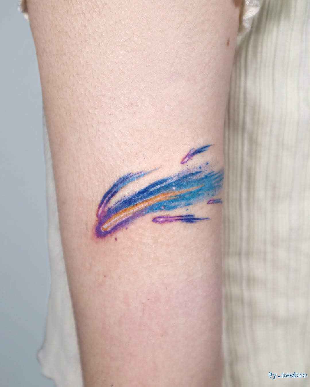 This meteor tattoo features a dynamic burst of colors, blending blues, purples, and hints of orange.
