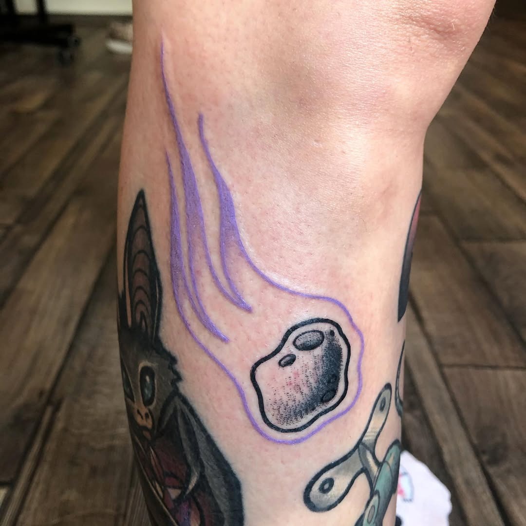 This tattoo features a playful meteor design with purple trailing waves.