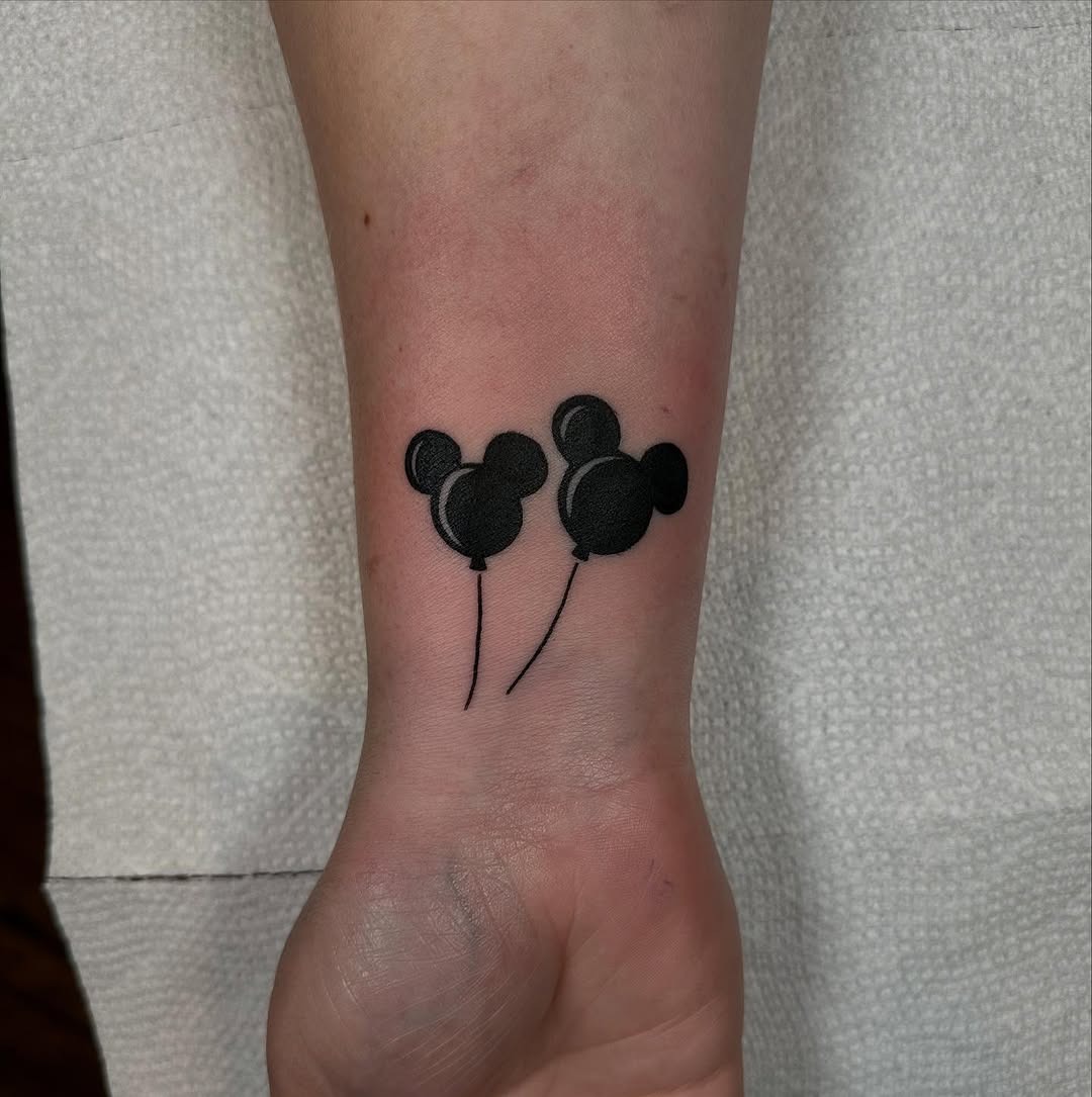This tattoo features two simplistic Mickey Mouse balloon designs, showing a playful and whimsical vibe.