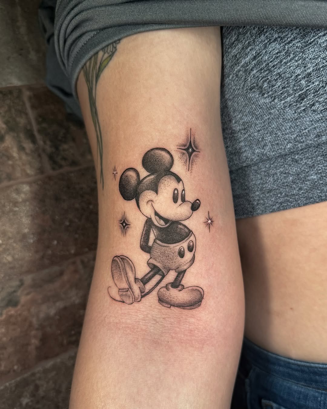 This tattoo features a timeless rendition of Mickey Mouse, portrayed in his iconic pose with a vintage flair.