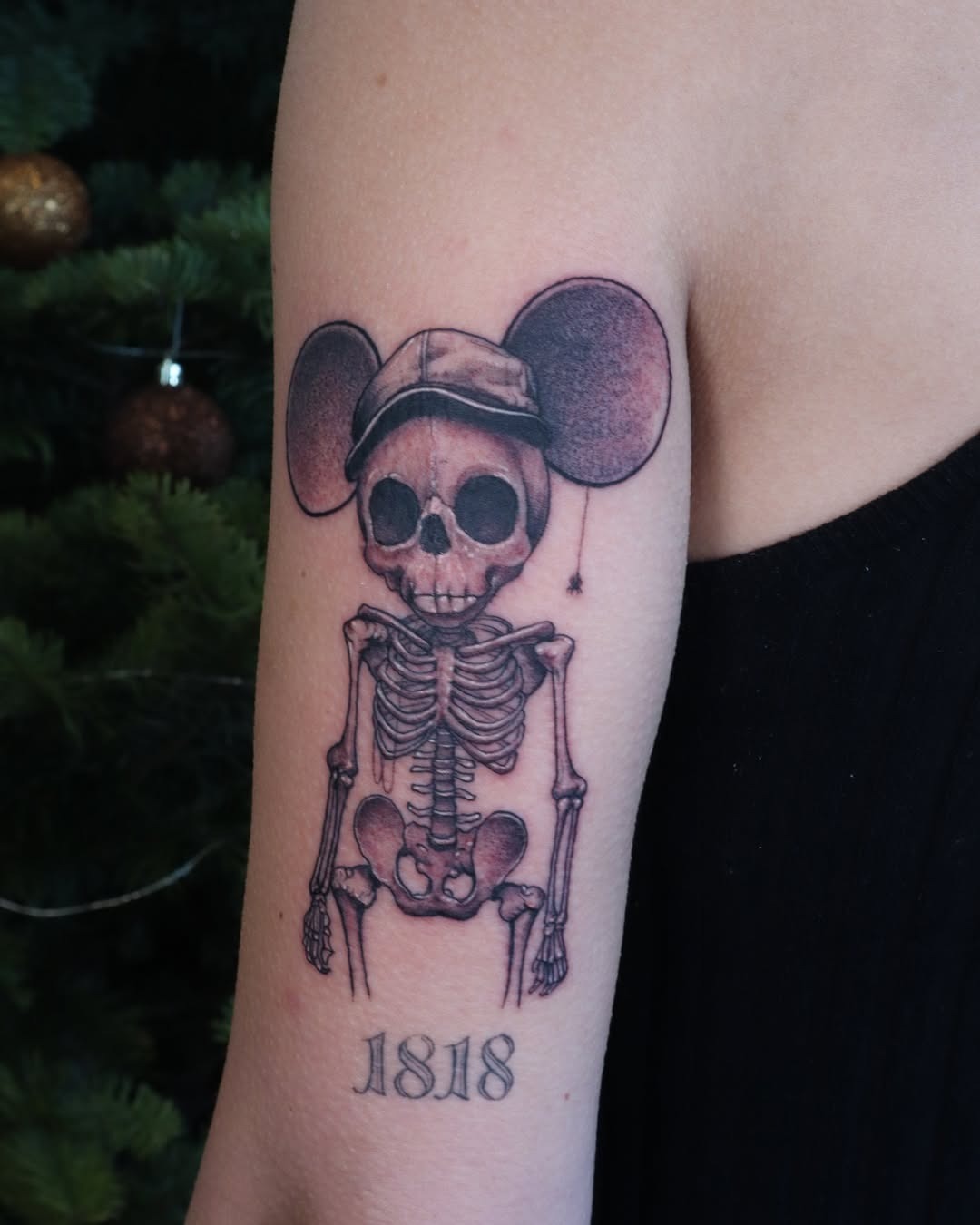 This tattoo depicts a playful spin on Mickey Mouse with a skeleton design, wearing a classic cap.