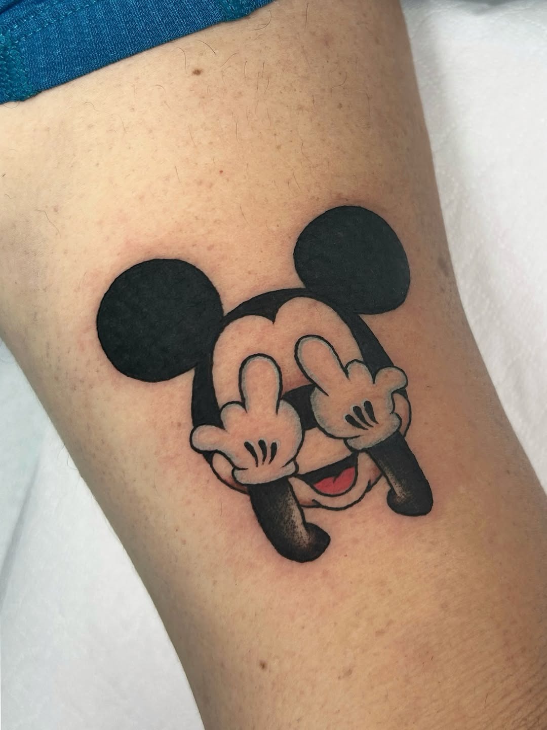 This tattoo features Mickey Mouse playfully showing the middle finger, blending humor with nostalgia.