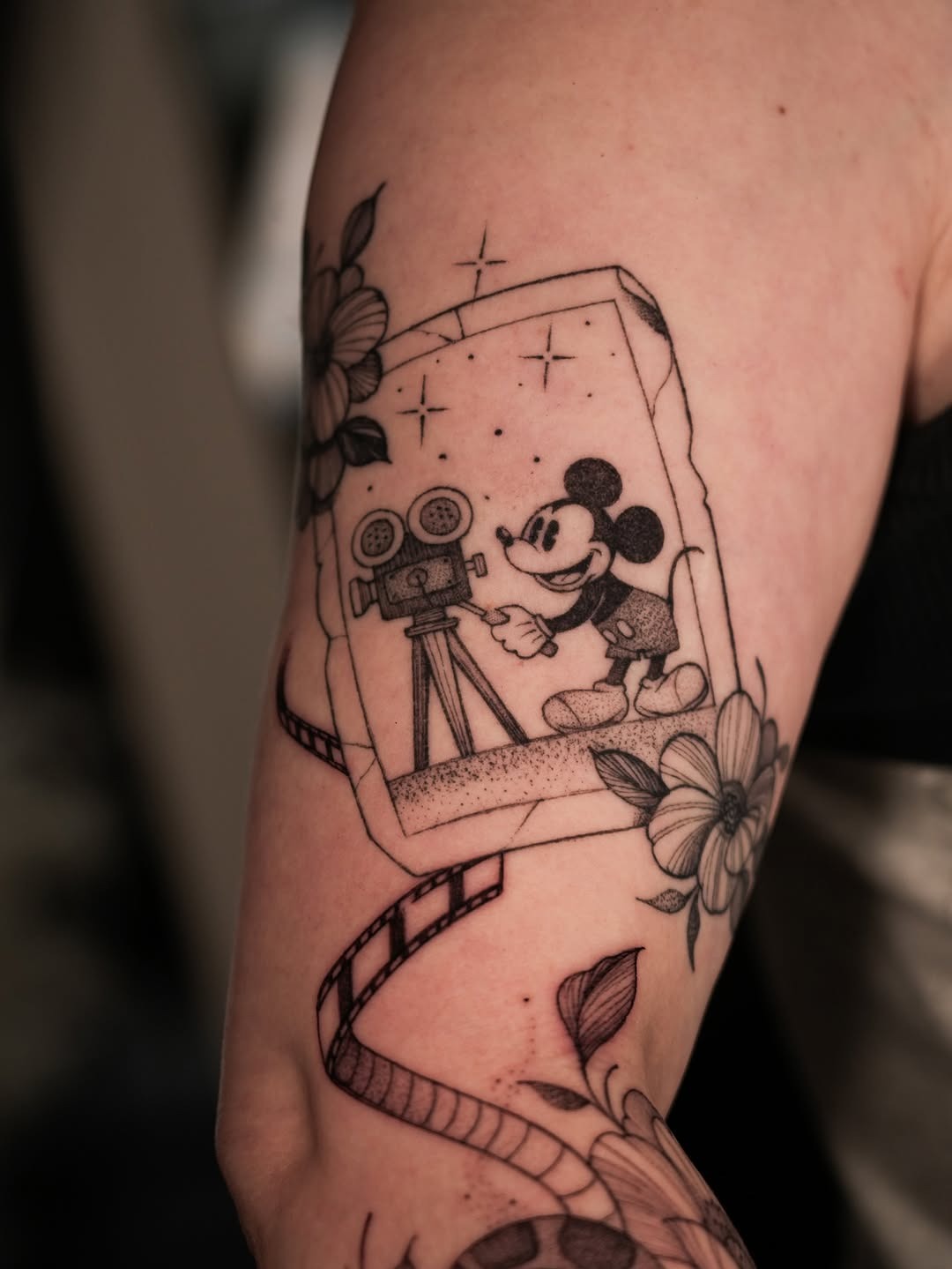 This tattoo features a playful Mickey Mouse in front of a vintage film camera captured in a charming frame.