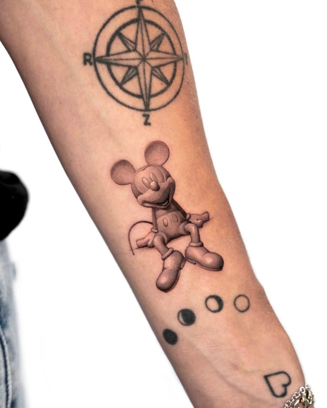 This tattoo showcases a whimsical Mickey Mouse in shades of black and gray.