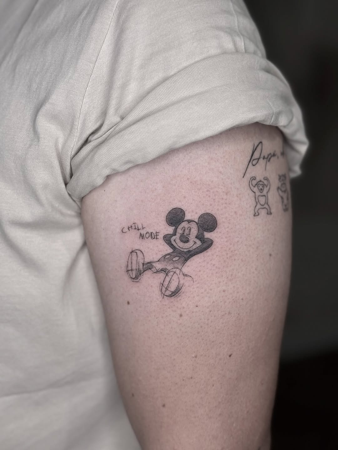 This tattoo features a playful Mickey Mouse lounging in a relaxed pose, exuding a carefree vibe.