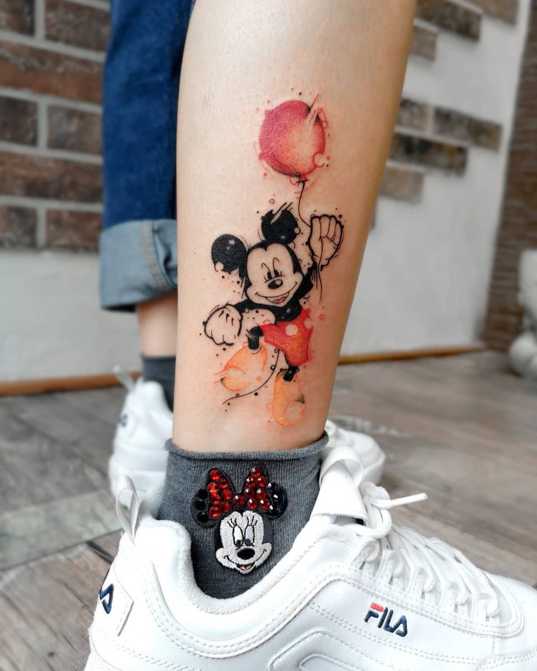 This tattoo features Mickey Mouse joyfully holding a red balloon, capturing a playful vibe.