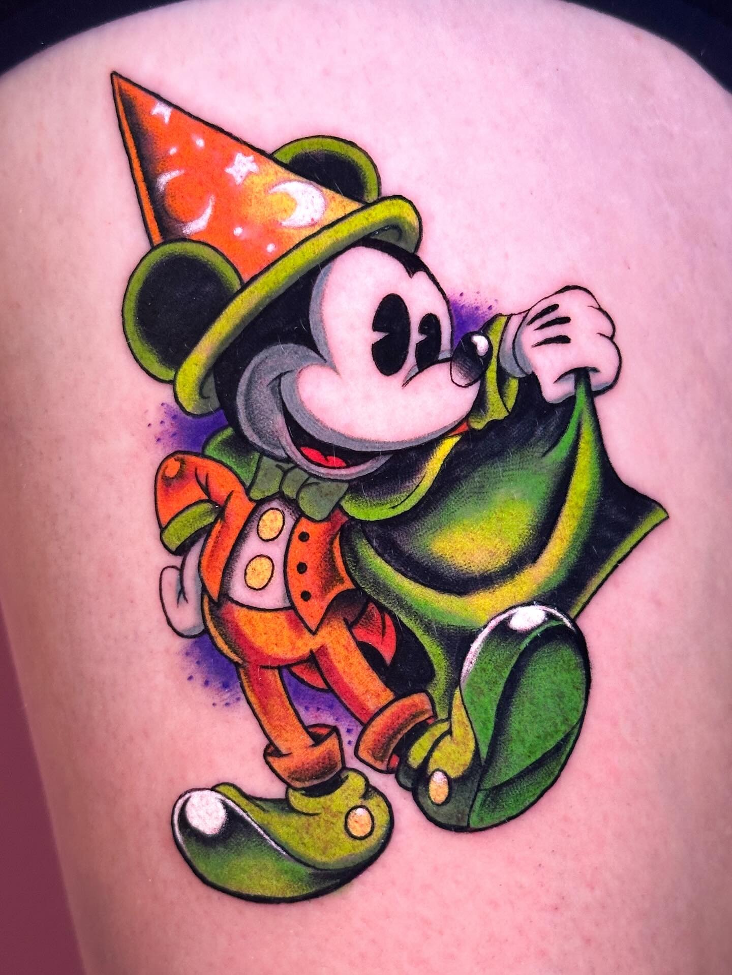 This tattoo features Mickey Mouse dressed as a magician, adorned in a colorful cape and hat.