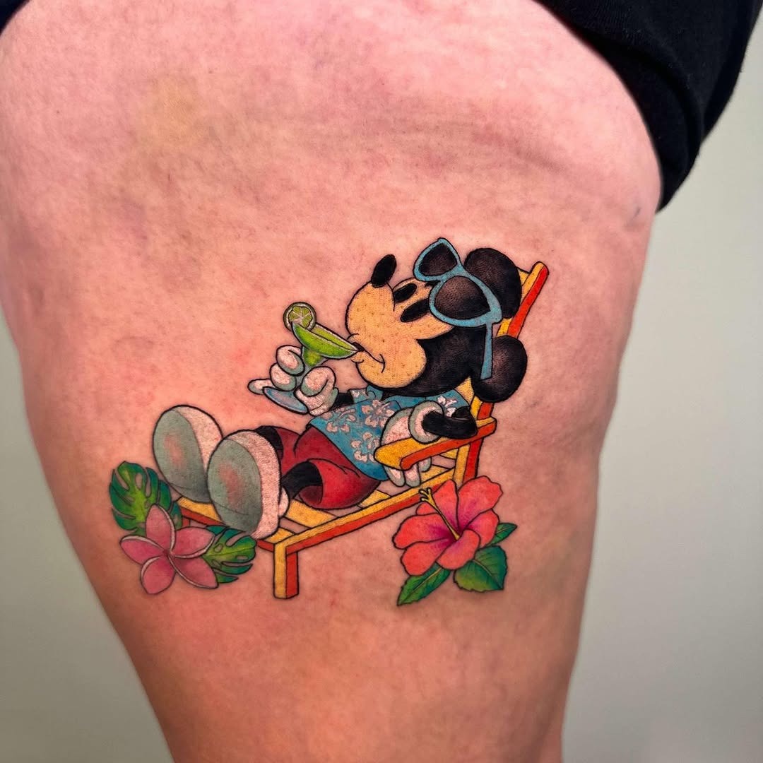 This tattoo showcases Mickey Mouse lounging in a beach chair, sipping a drink.