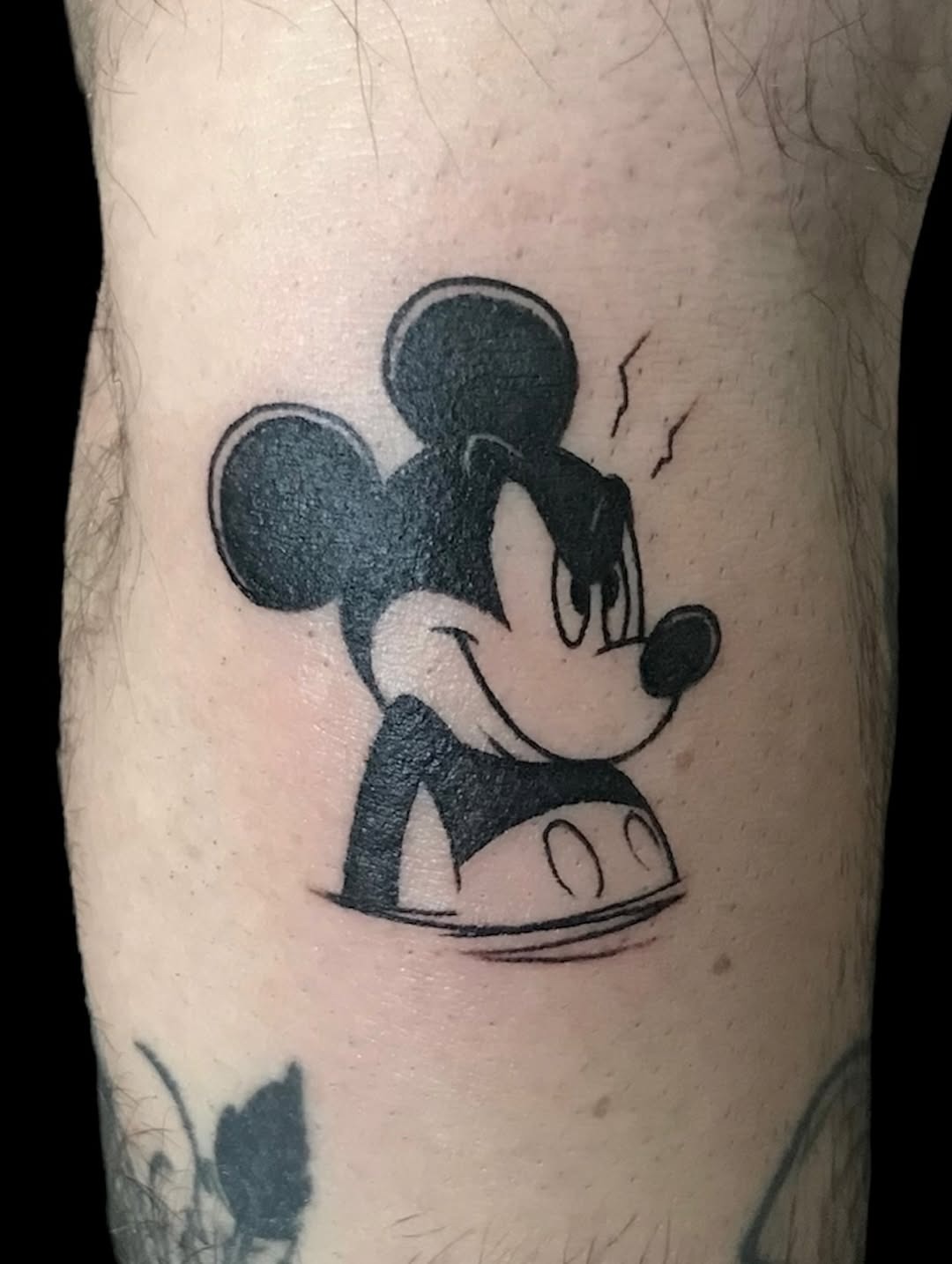 This tattoo features a classic Mickey Mouse design with sharp, bold lines.