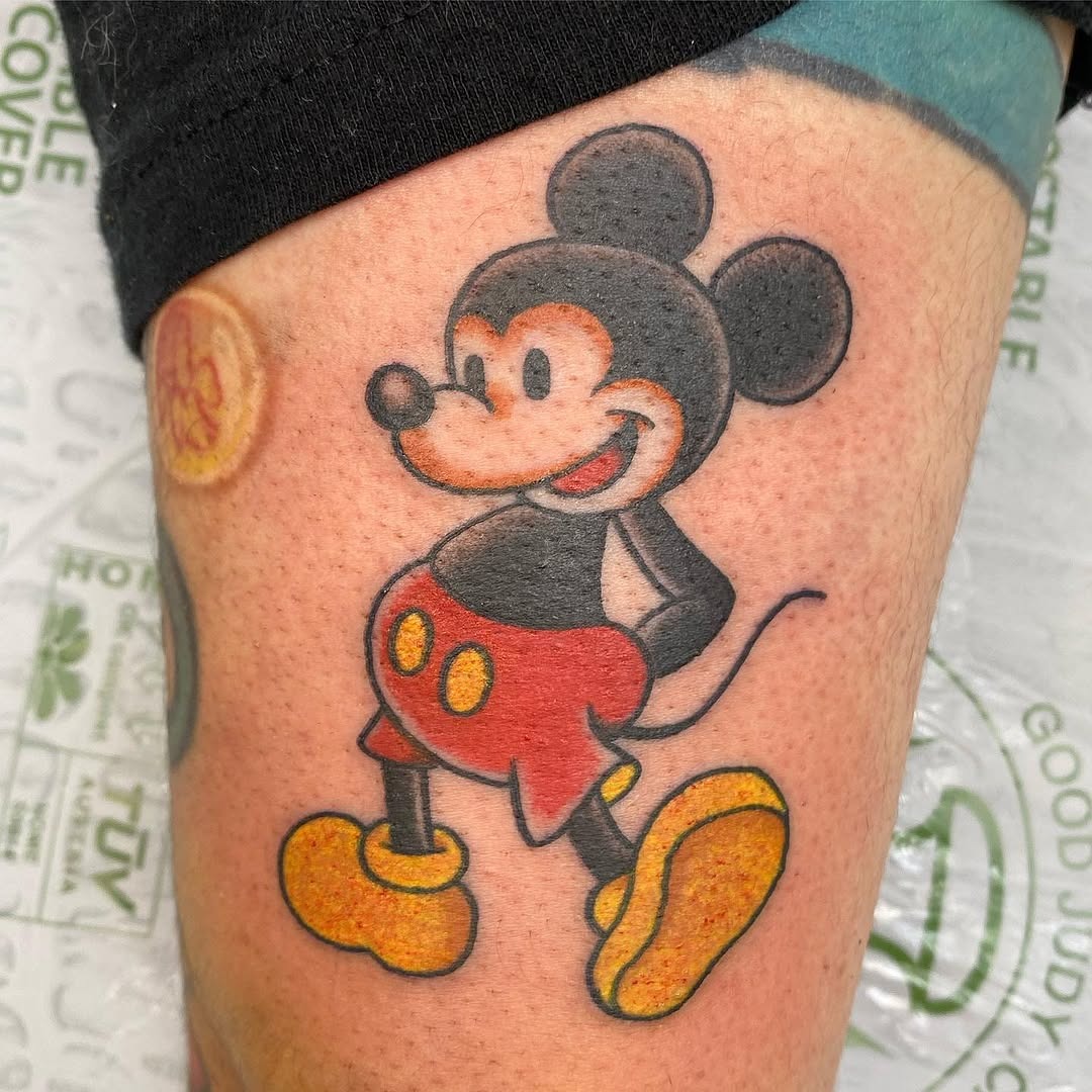 This tattoo showcases a cheerful Mickey Mouse in his iconic pose.