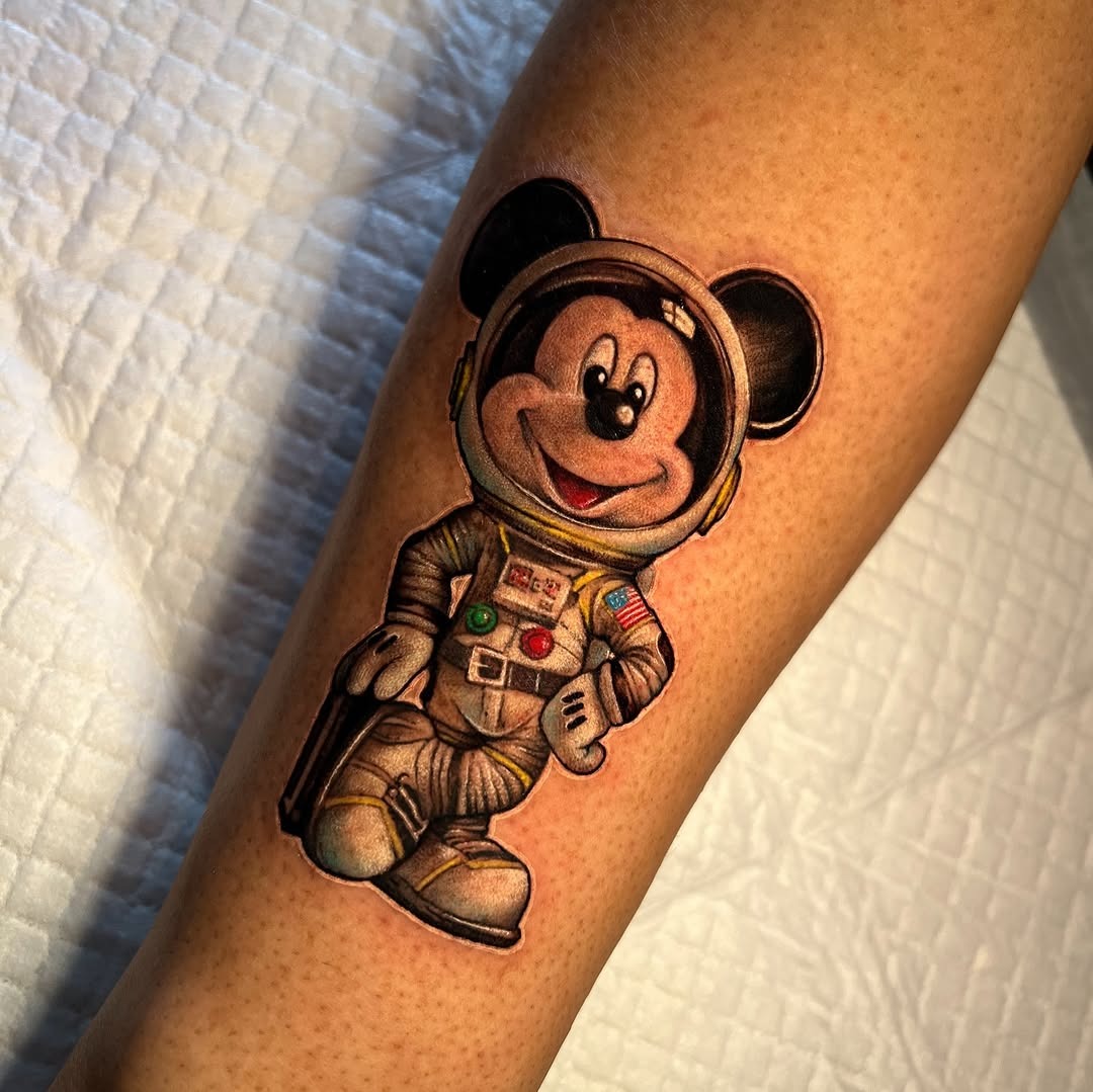 This tattoo features Mickey Mouse dressed as an astronaut, complete with a helmet and space suit.