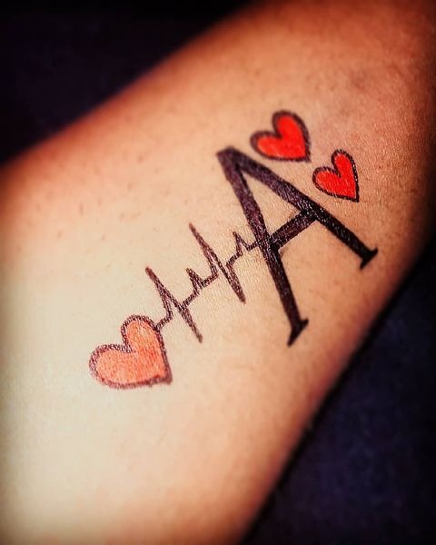 Incorporating red hearts around a stylized letter A, this tattoo on the arm is rich with symbolism and visual appeal.