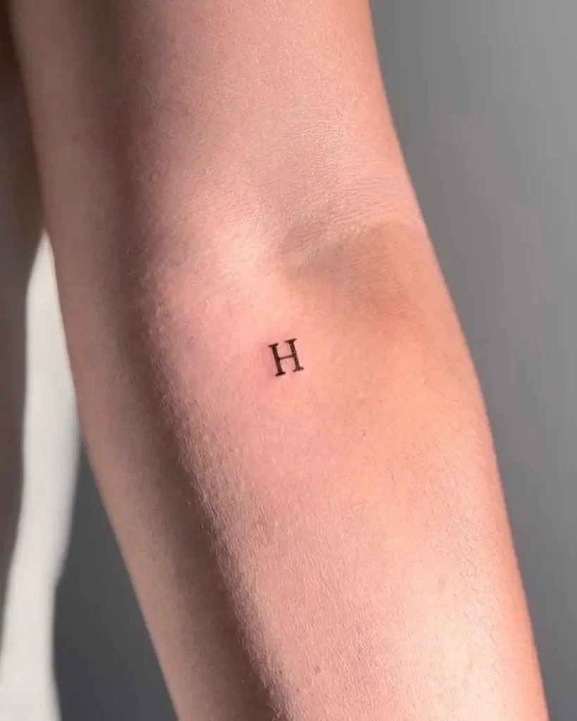 The simplicity of a single, bold letter H tattooed on the inner forearm represents a trend towards minimalist tattoo choices.