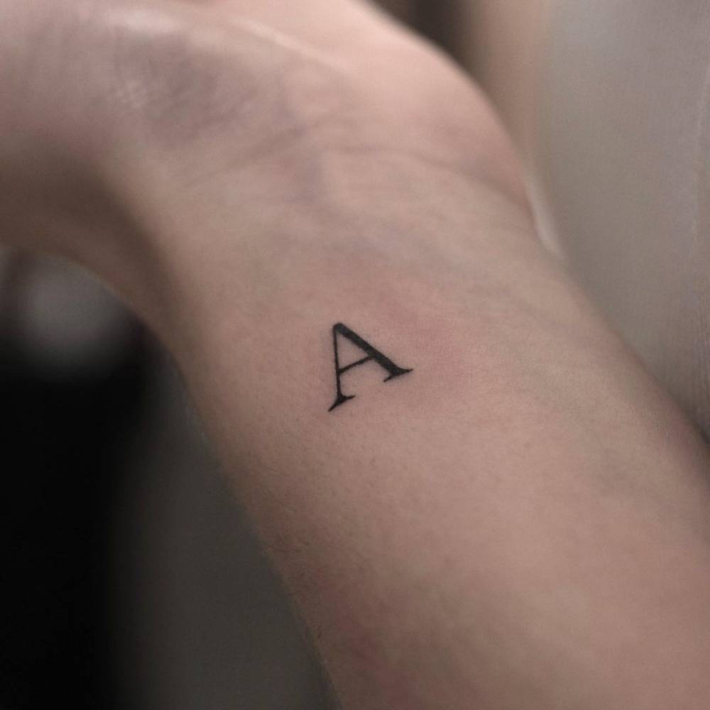 A stark, minimalist letter A tattooed on the arm represents the essence of modern tattoo trends, simple and direct.