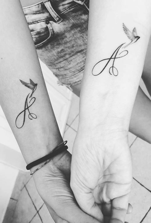 Showing a creative design, two letter As are inked on each person's wrist, joined by an artistic rendering of flying birds.
