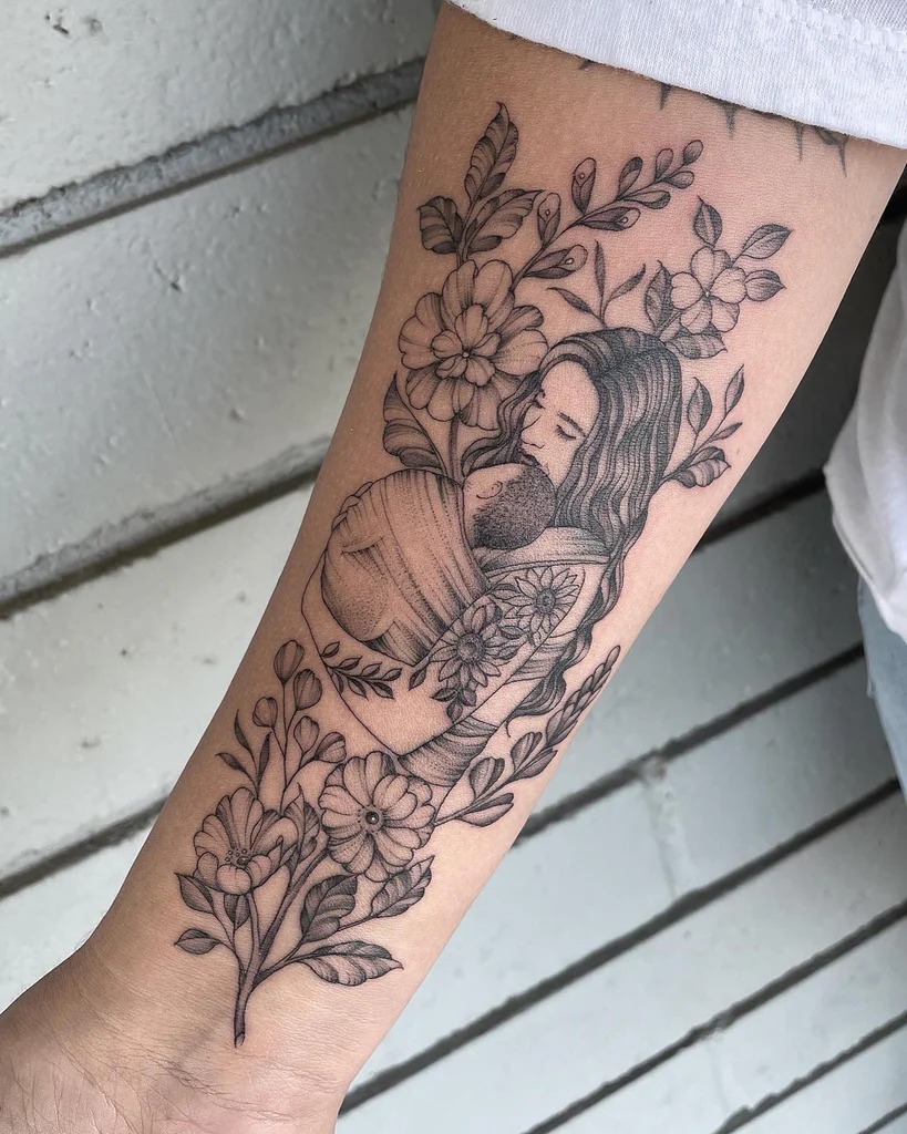 This tattoo captures a tender moment between a mother and her child, surrounded by an intricate floral design.