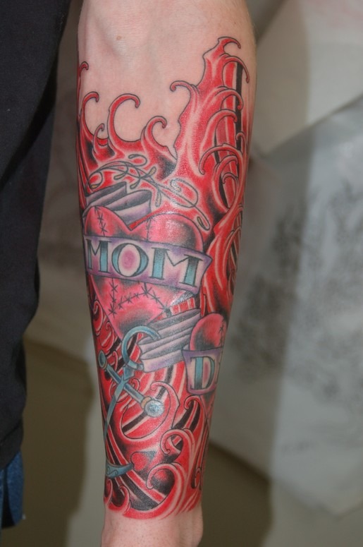 This tattoo features a bold red heart with the words "Mom" and "Dad" wrapped in a banner, anchored by a traditional tattoo-style anchor.
