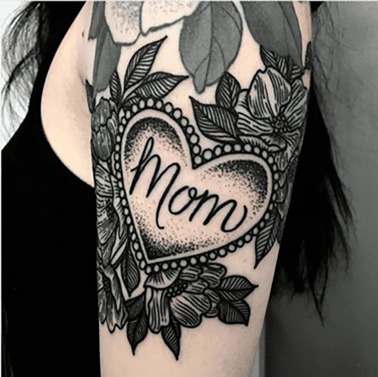 Incorporating the word "Mom" within a heart-shaped frame, this tattoo is surrounded by beautifully detailed flowers.