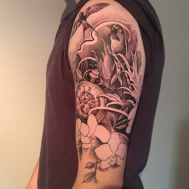 This sleeve tattoo combines elements of nature with timeless symbols, showing birds perched among lush foliage and a classic pocket watch.