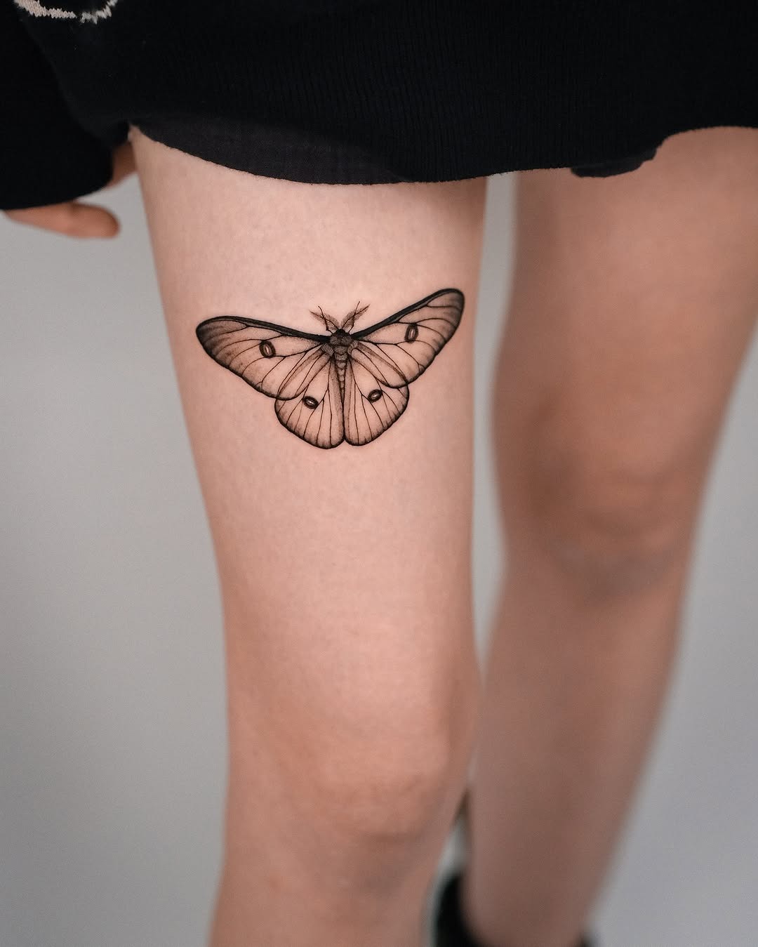 Elegant black line moth tattoo on thigh Tattoo Design