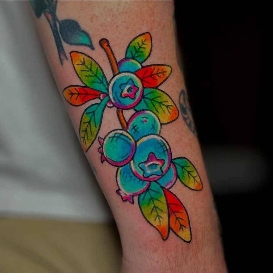 This tattoo features a blueberry branch adorned with lush green leaves.