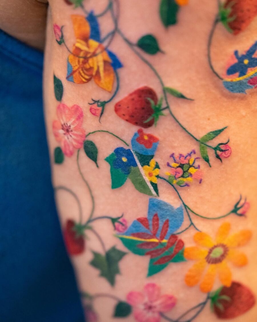 This tattoo showcases a playful mix of colorful flowers and strawberries intertwined with green vines.