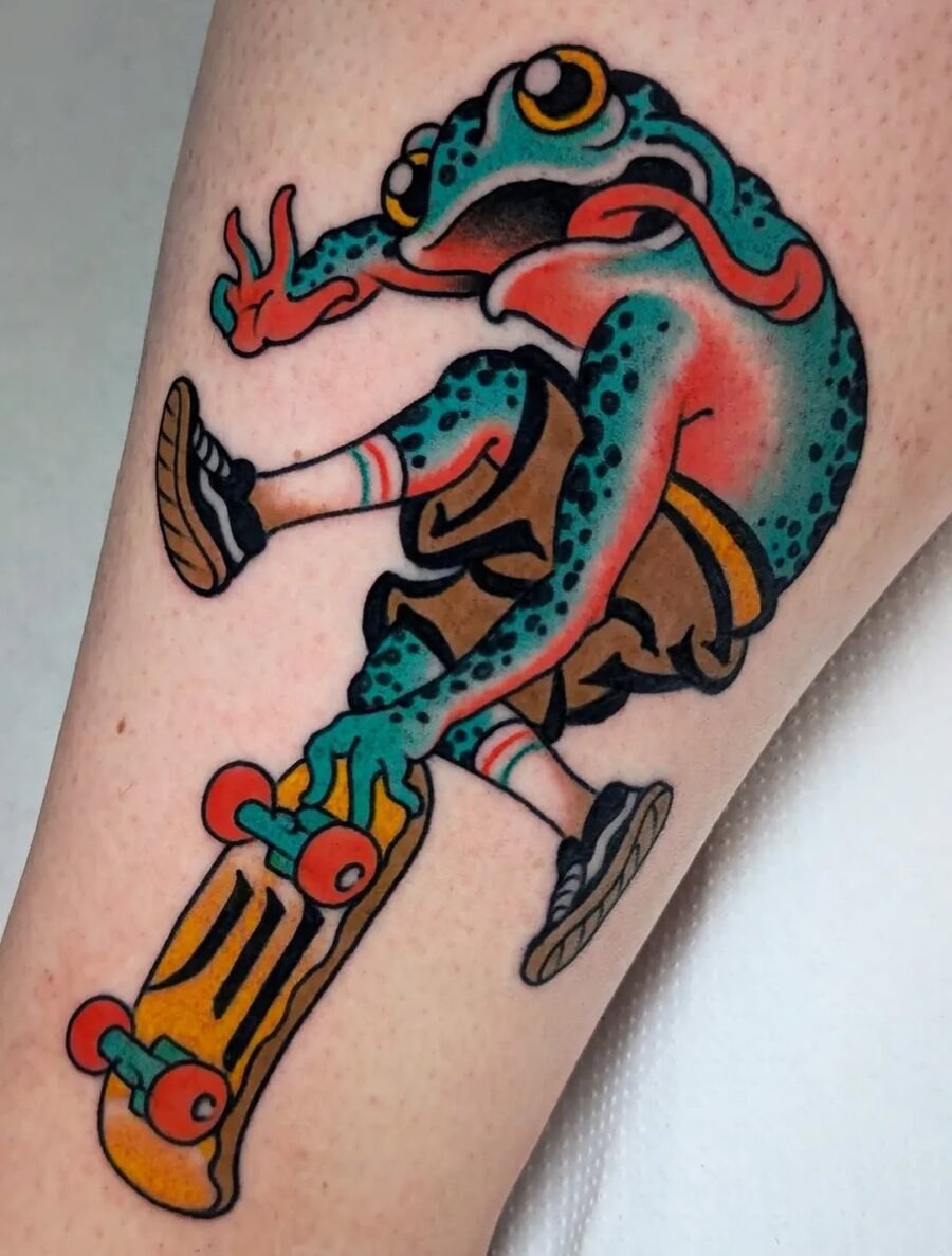 This tattoo features a lively frog performing a skateboard trick.