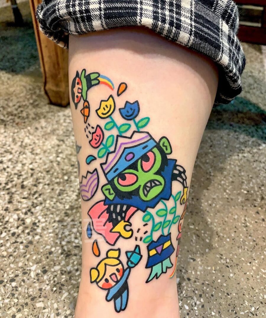 This playful tattoo showcases a green creature surrounded by colorful flowers and whimsical characters.