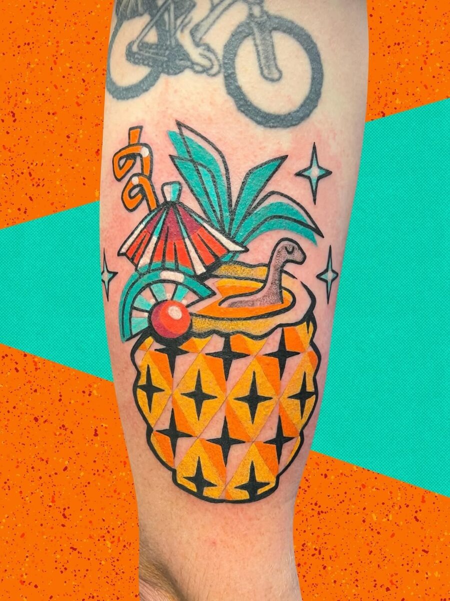 This new school tattoo features a playful pineapple cocktail adorned with an umbrella and a whimsical snake.