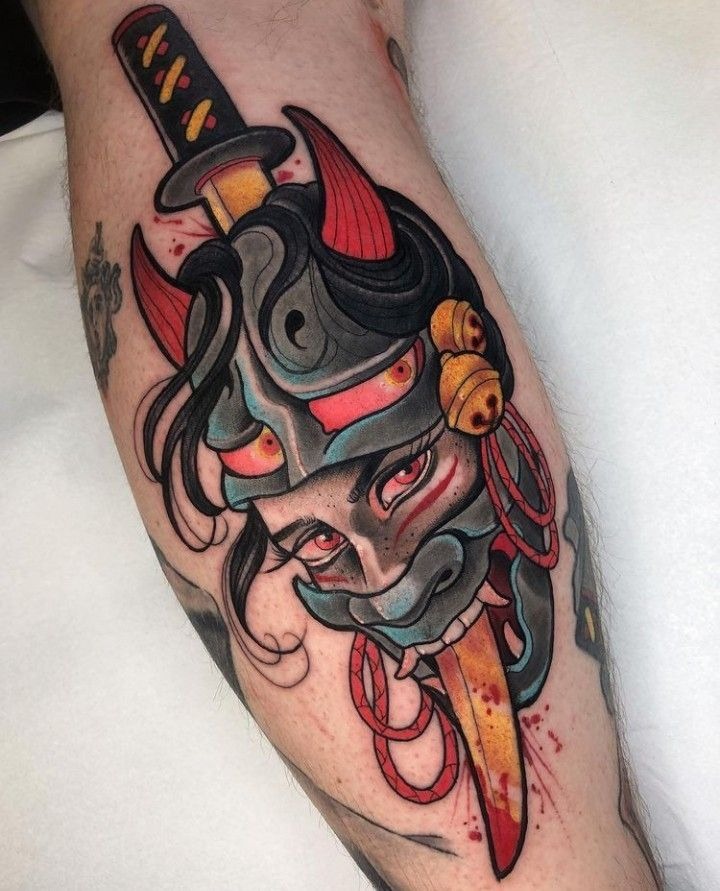 Playful yet bold, this calf tattoo introduces a female face peeking through an oni mask, accented by a dagger.