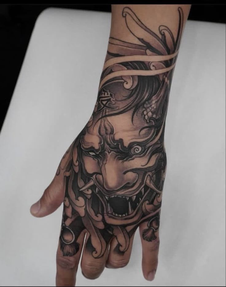 This inky hand piece merges an oni's face with organic, flowing motifs that stretch across the fingers and wrist.