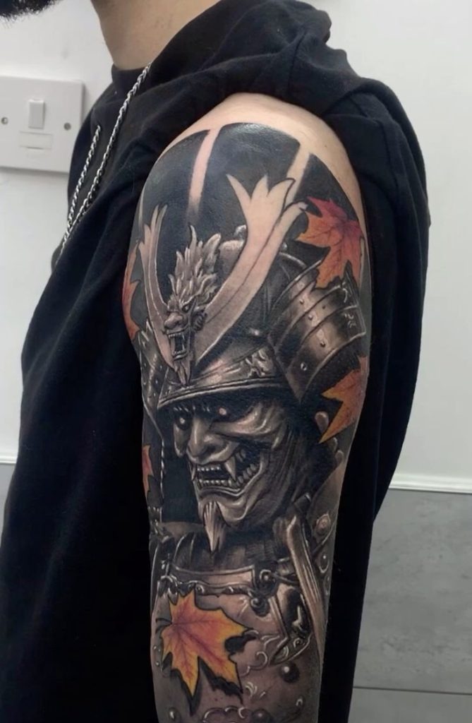 A powerful fusion of samurai armor and oni mask creates this deeply detailed sleeve tattoo that wraps the upper arm in dark steel and legend.