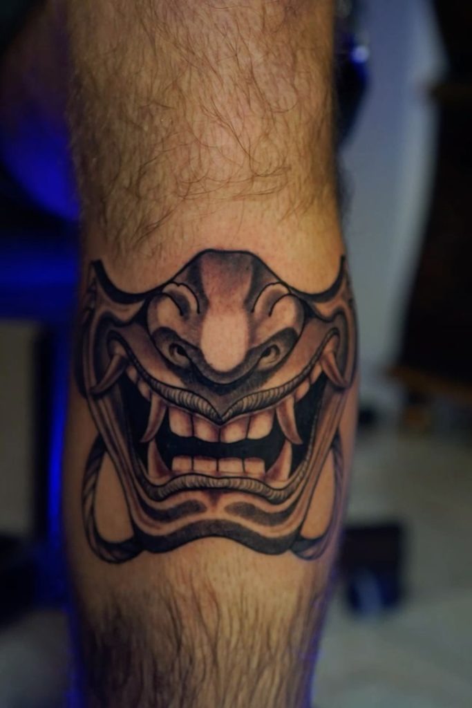Classic in execution, this leg tattoo goes back to basics with a strong, grinning oni mask that wraps around the calf muscle like armor.