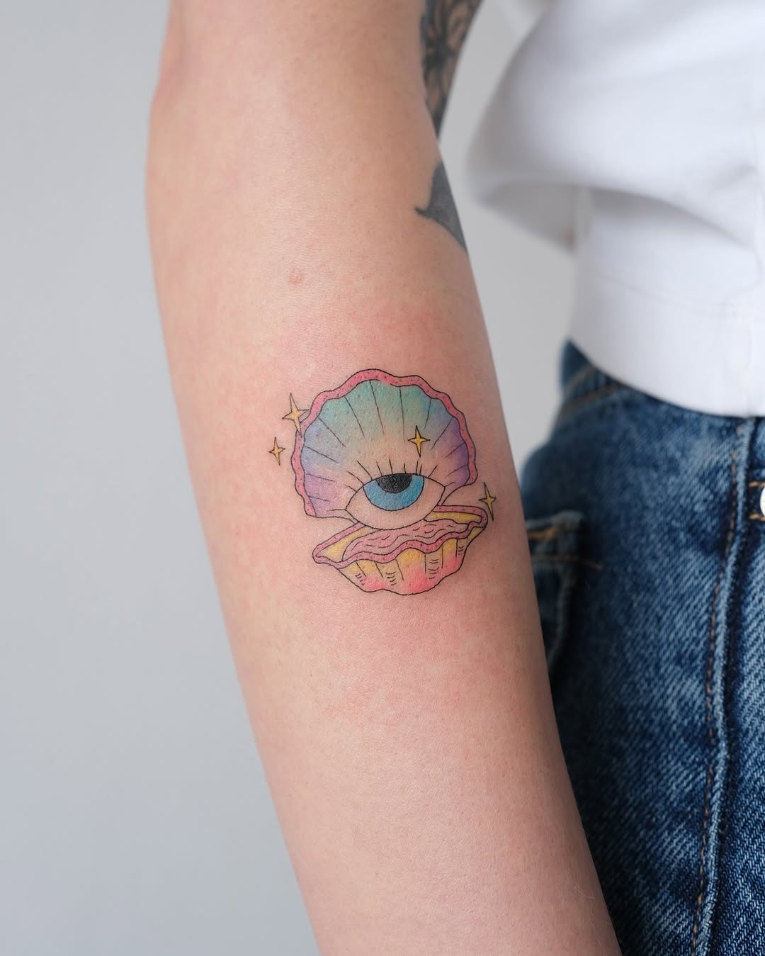 This tattoo showcases a colorful oyster shell, elegantly closed with a mystical eye peeking through.