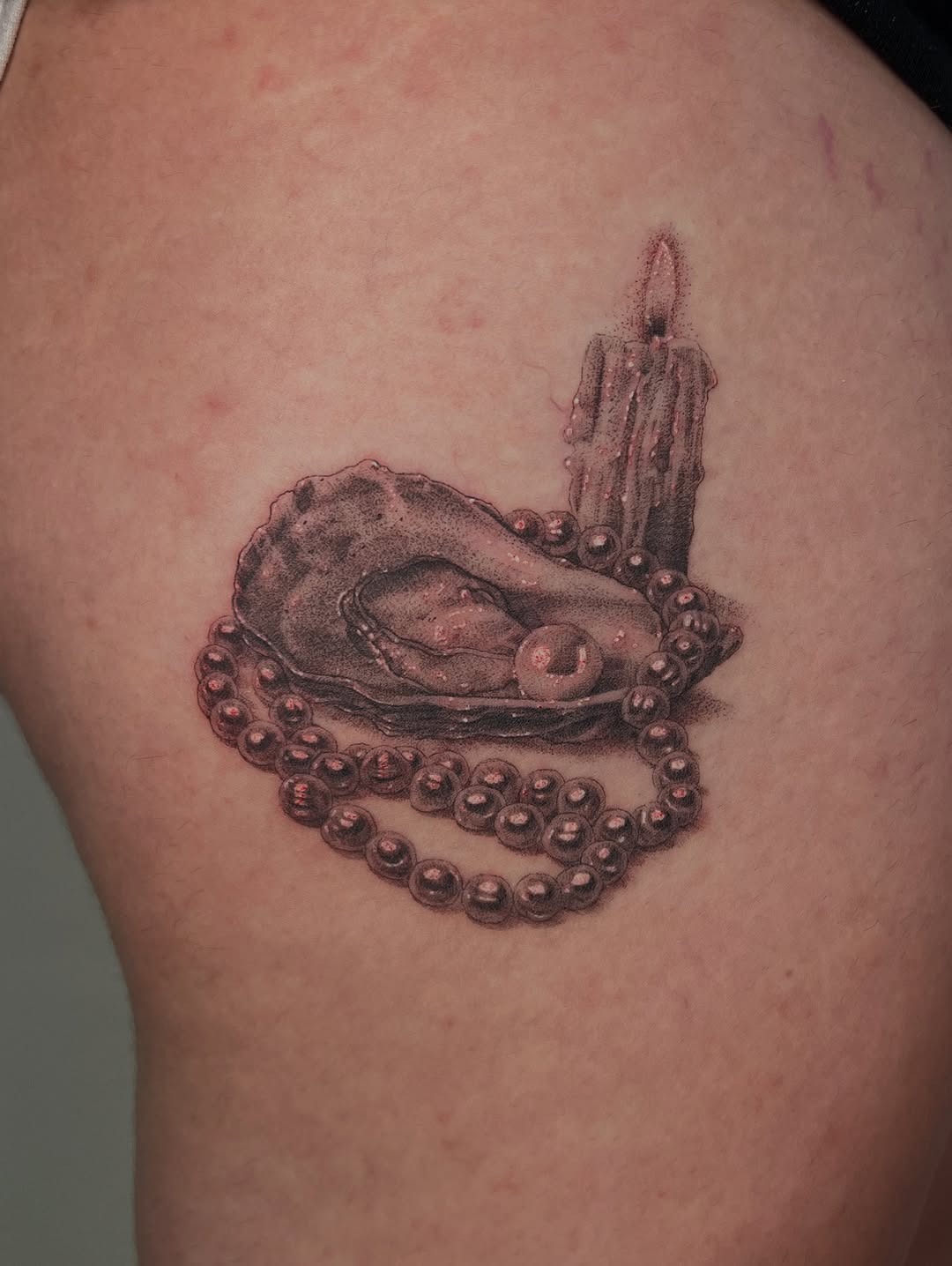 This tattoo beautifully combines an oyster with a pearl nestled inside, surrounded by intricate beads and a candle.