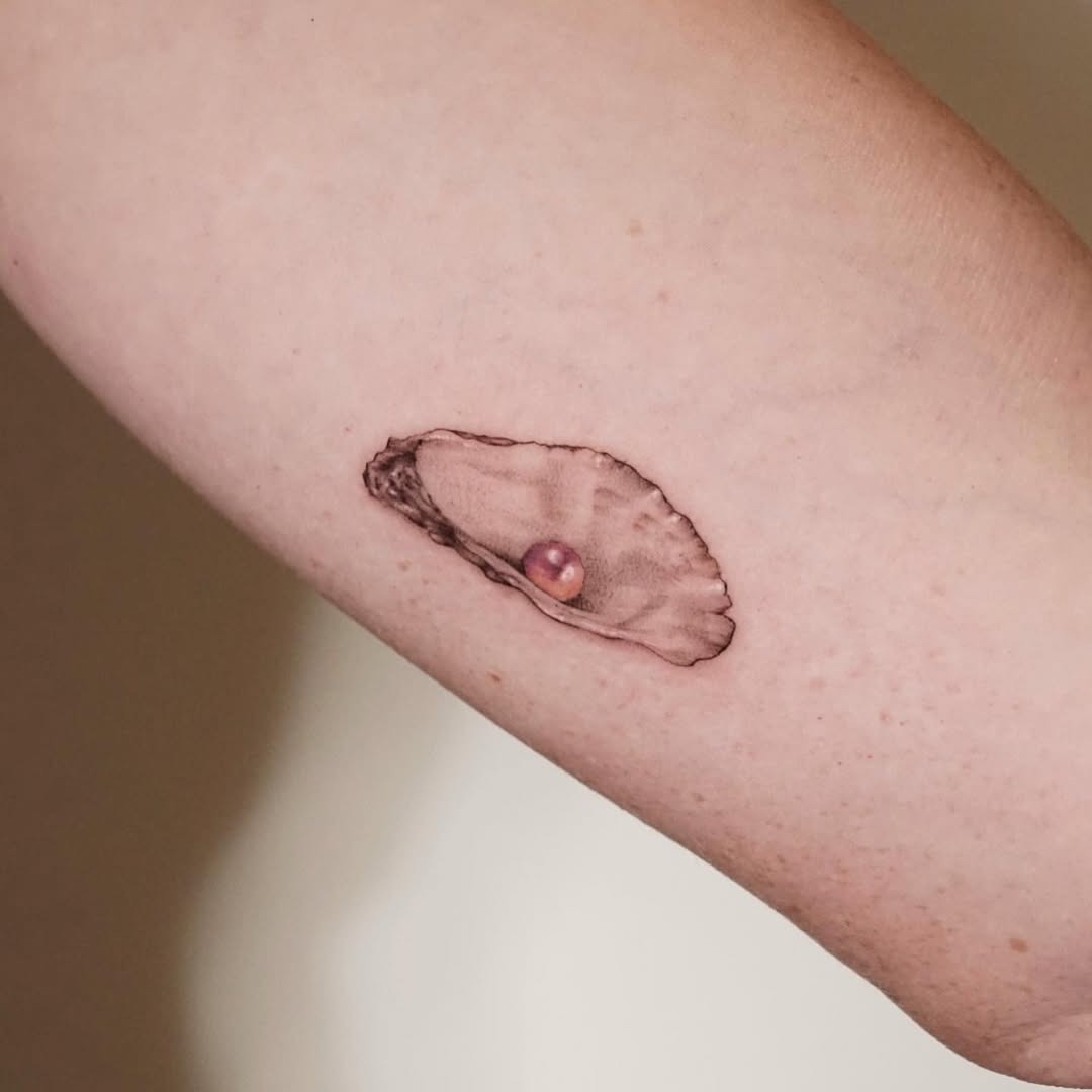 This tattoo features a stunningly realistic oyster resting on the skin, complete with a shiny pearl nestled inside.