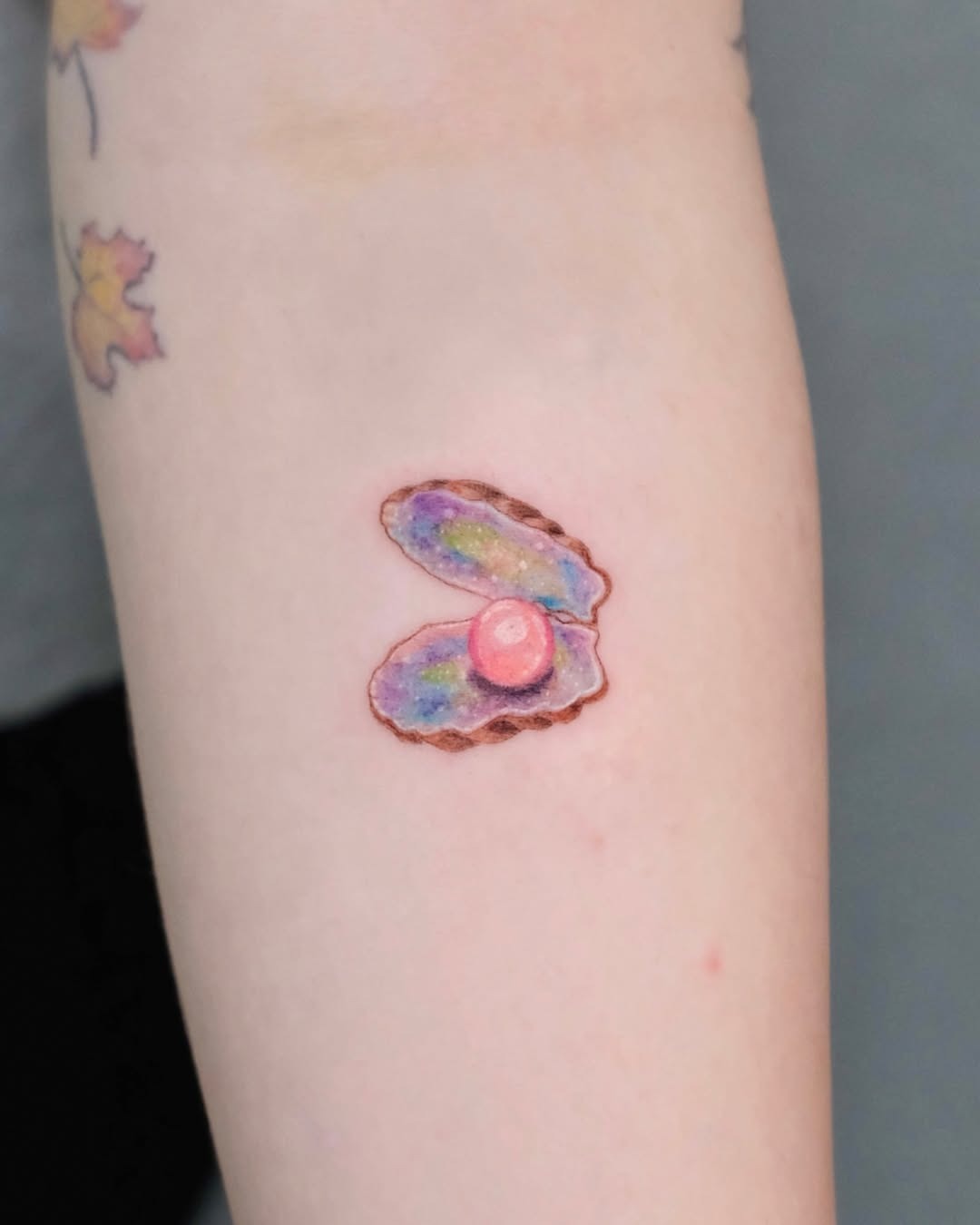 This tattoo features a beautifully designed oyster with an iridescent pearl nestled inside.