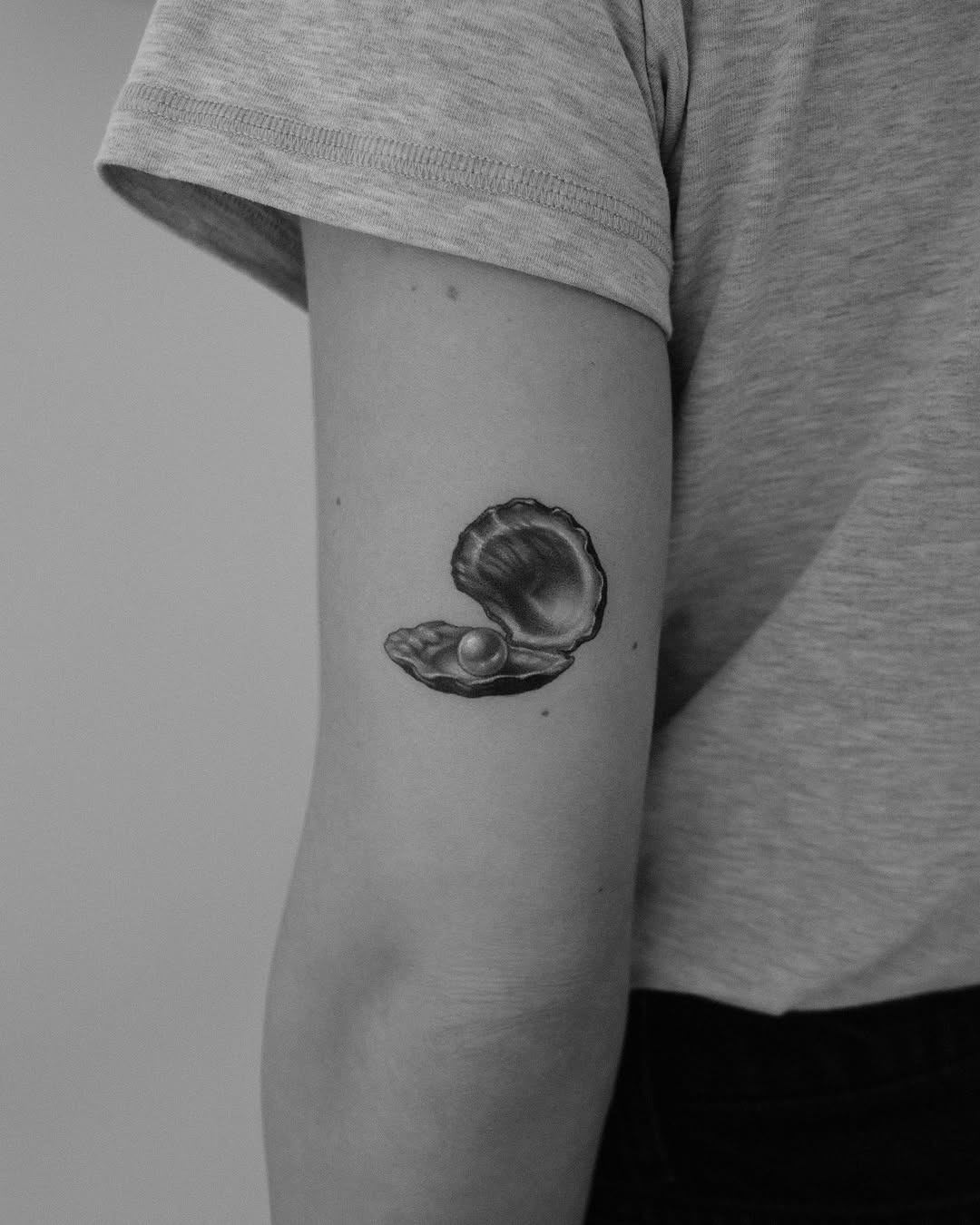 This tattoo showcases a beautifully detailed oyster shell, slightly ajar to reveal a gleaming pearl inside.
