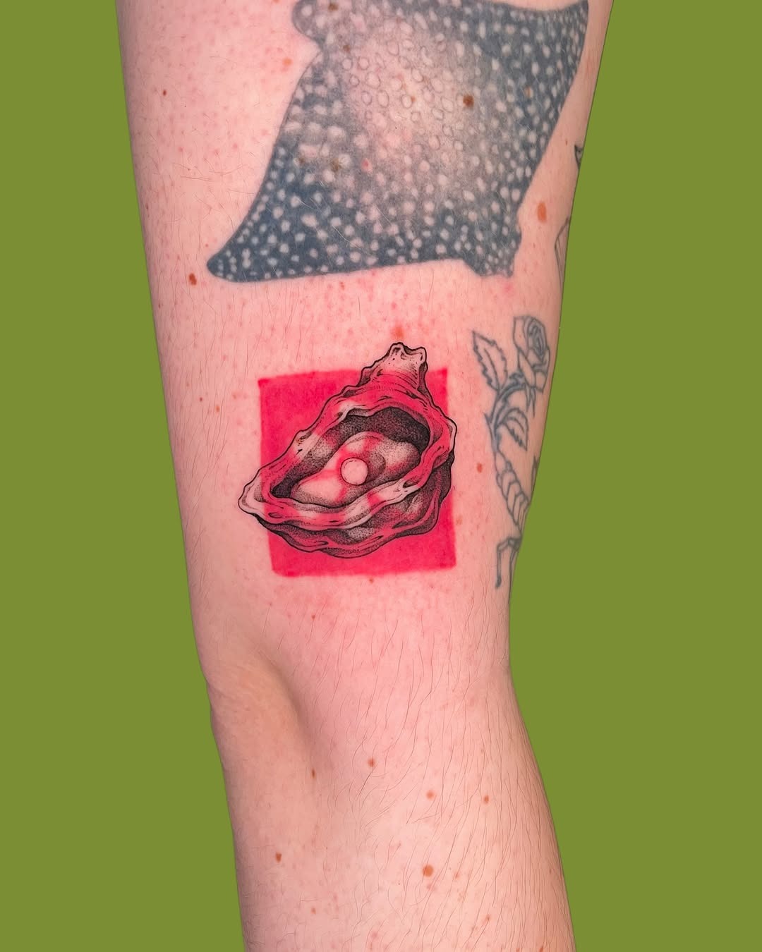This tattoo showcases a beautifully detailed oyster on a striking red background.