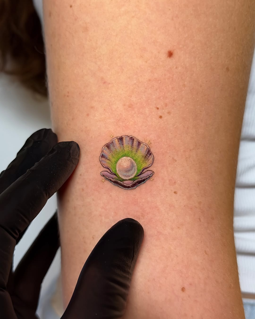 This tattoo features a beautifully detailed oyster shell prominently displaying a pearl in the center.