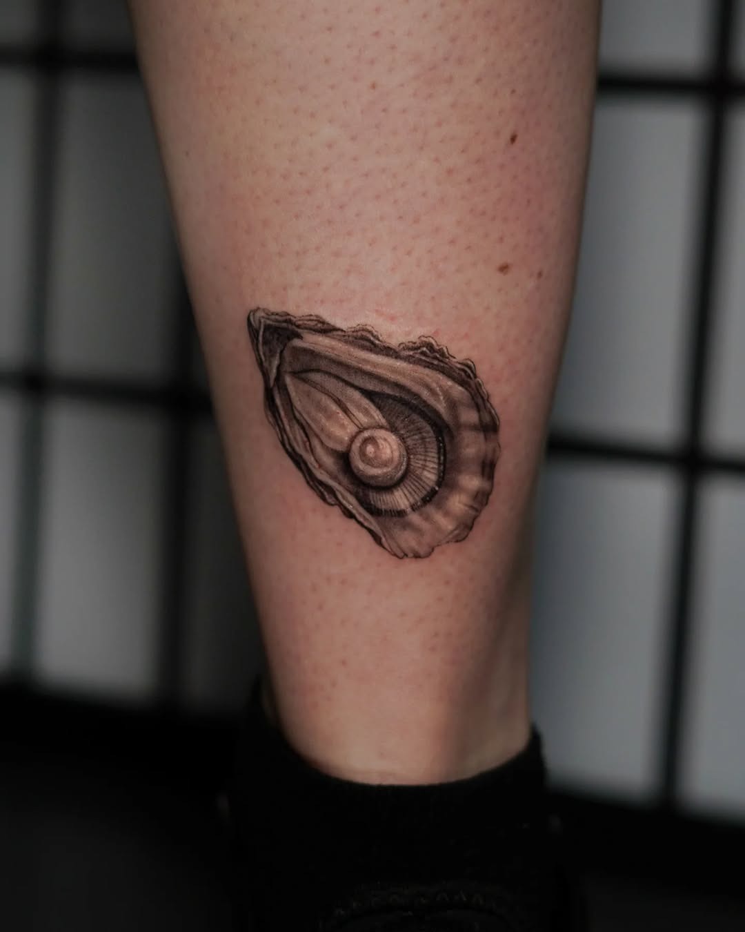This tattoo features a beautifully detailed oyster shell prominently displaying a pearl in the center.