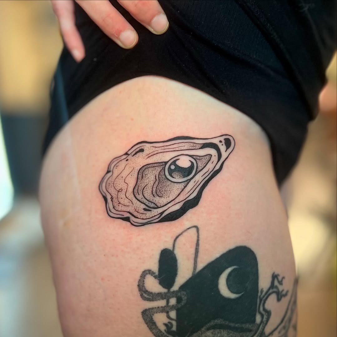 This tattoo features a beautifully detailed oyster design, emphasizing its smooth contours.