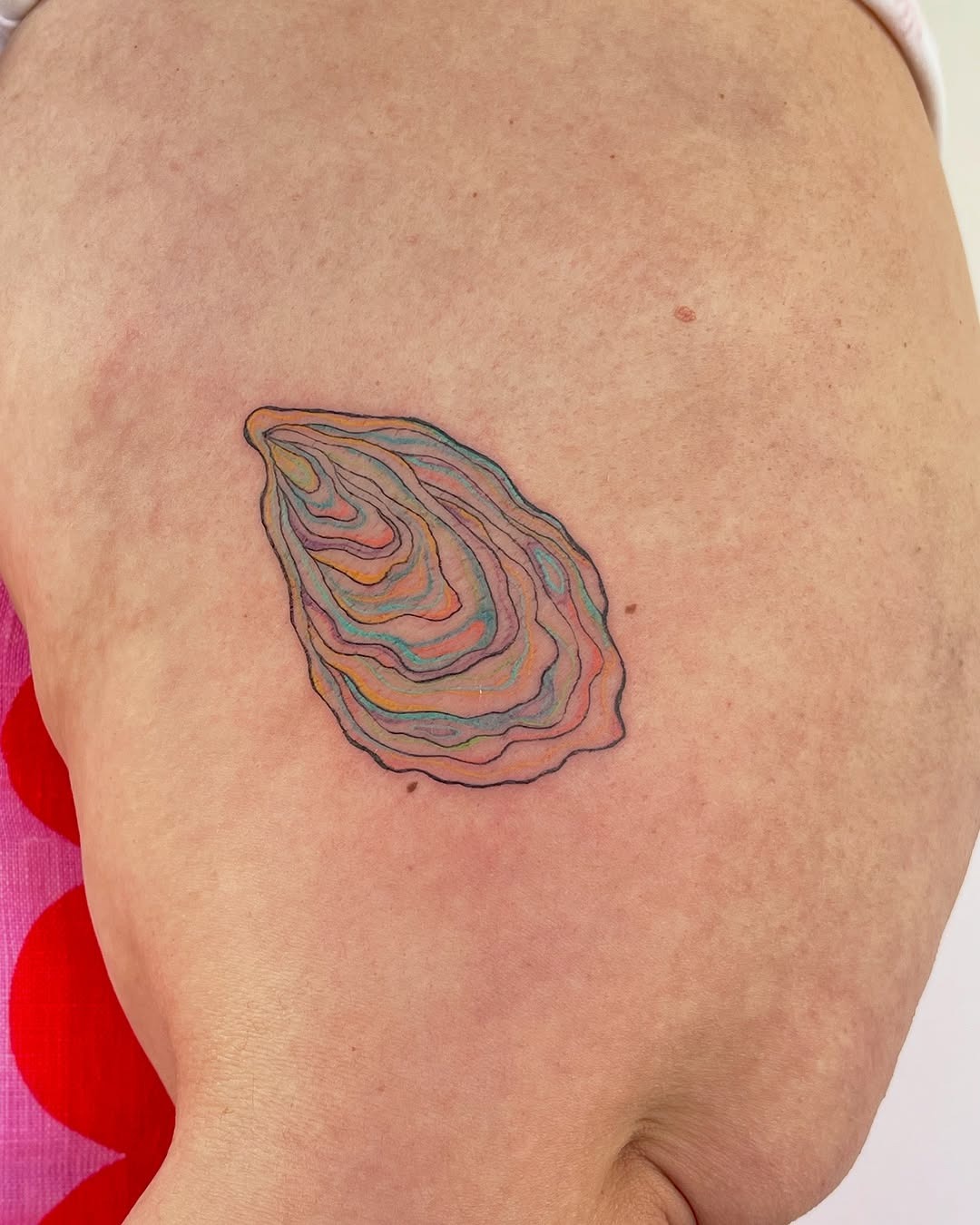 This tattoo showcases a beautifully stylized oyster with, swirling colors.