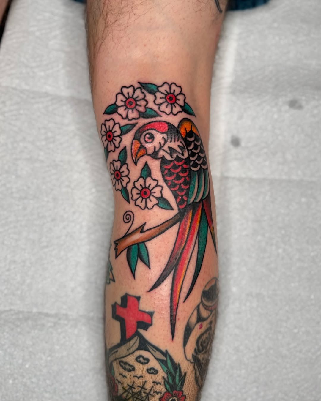 Vibrant parrot tattoo adorned with blossoms Tattoo Design