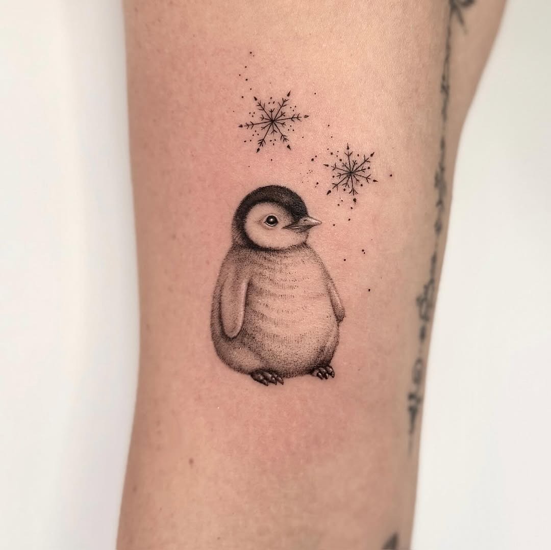 Charming penguin tattoo surrounded by snowflakes. Tattoo Design